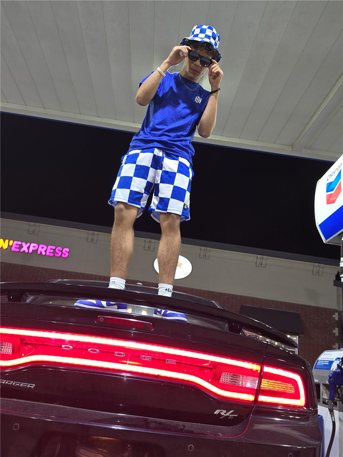 Status and Stitches customer standing on a Dodge Charger in Home Grown checkered gear